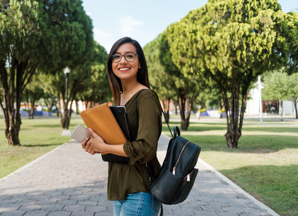 Female student posing on stone sidewalk holder a laptop and folder.